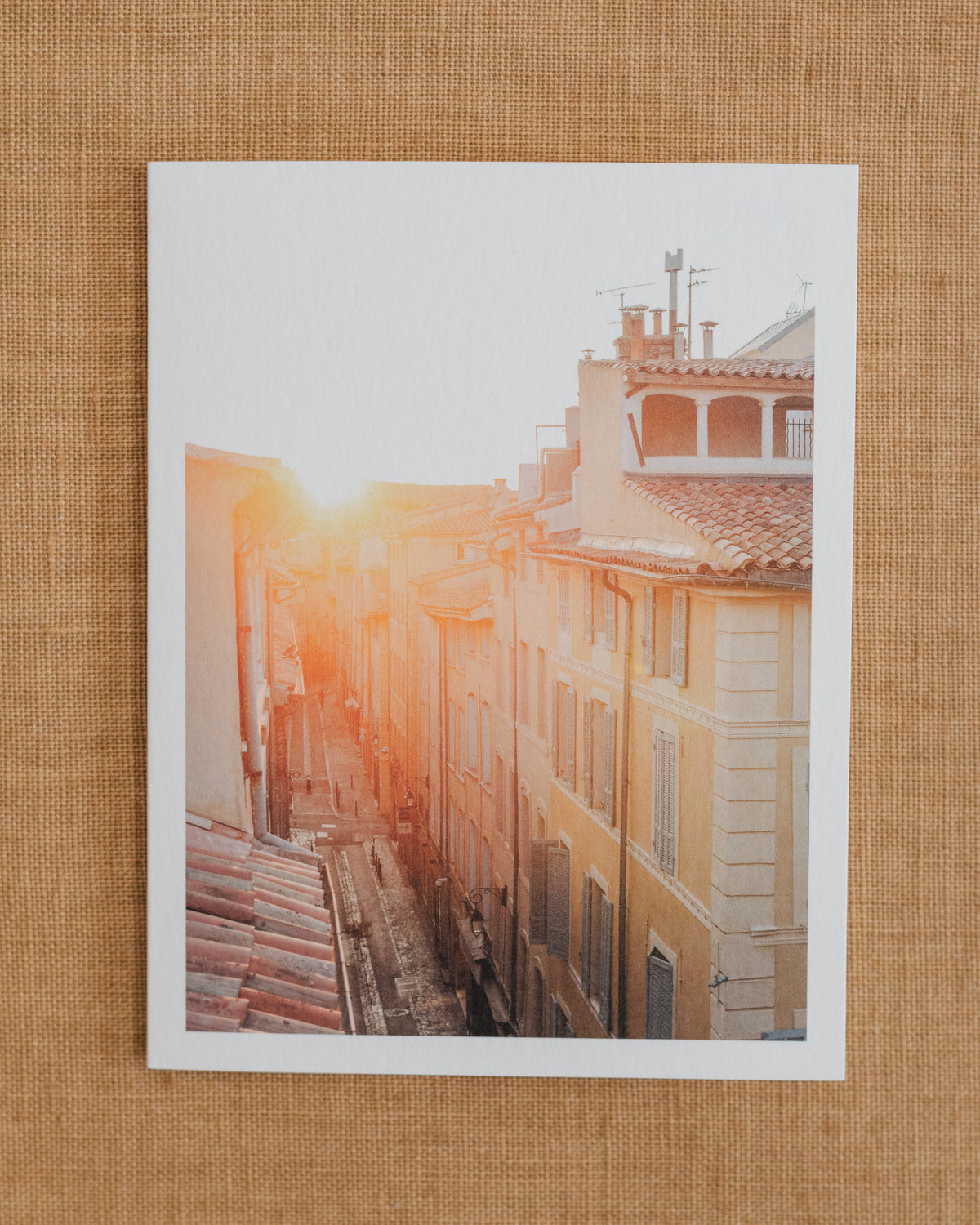 Photographic notecard showing golden sunrise over rooftops and a narrow street in Aix, Provence.