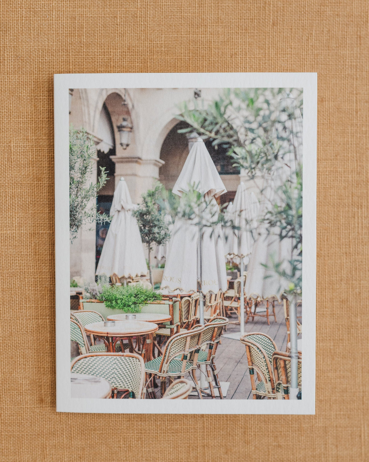 Paris café photographic notecard featuring woven chairs, white umbrellas, and greenery.