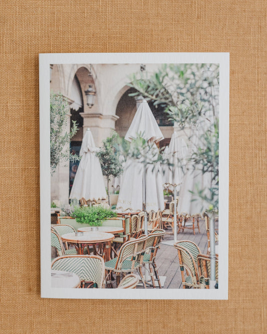 Paris café photographic notecard featuring woven chairs, white umbrellas, and greenery.
