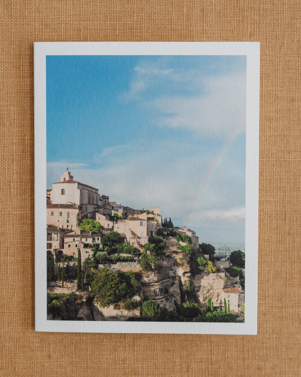 Photographic notecard showing a rainbow above a hillside village in Provence.
