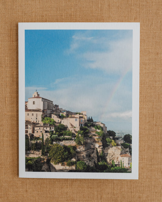 Photographic notecard showing a rainbow above a hillside village in Provence.